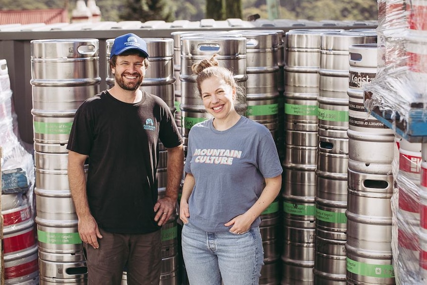 Un uomo e una donna in piedi davanti a fusti di birra in metallo.