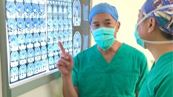 一名身穿手术装备的男子指着显示 X 射线的屏幕
