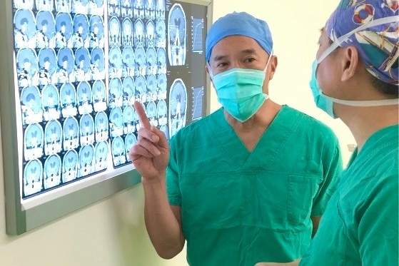 a man wearing surgical gear pointing to a screen showing x arays