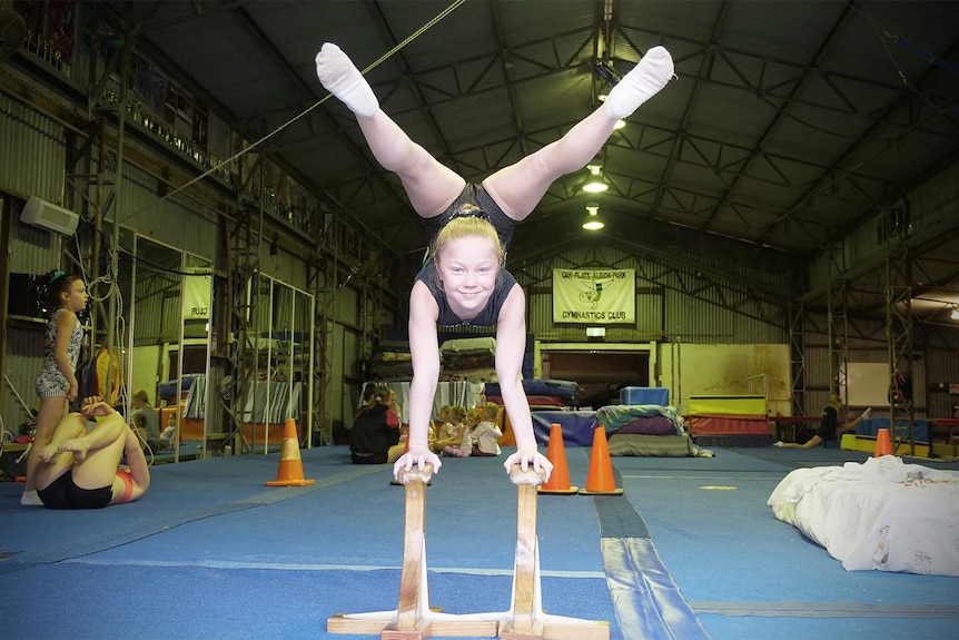 Paytience Hesse performs a hand stand with her legs up and over her head while smiling at the camera.