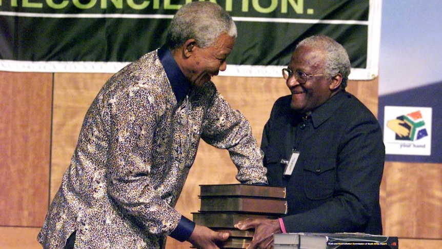 Nelson Mandela accepts stacked books of the Truth and Reconciliation Commission's report from Archbishop Desmond Tutu.