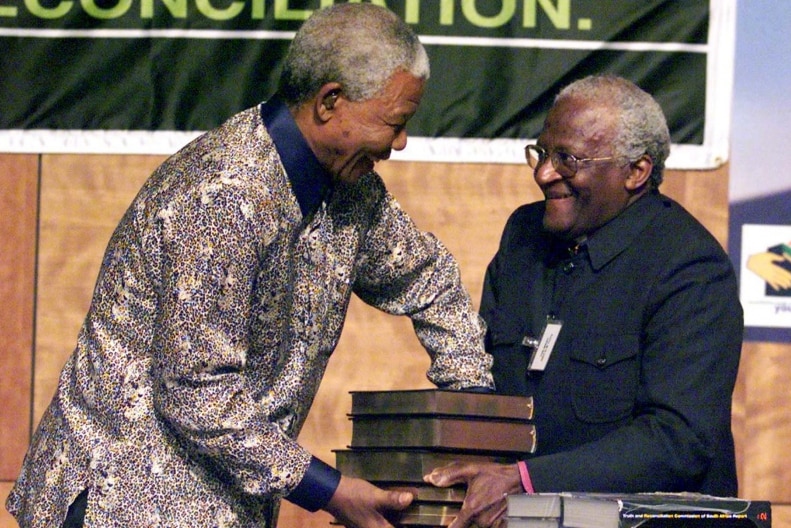 Nelson Mandela accepts stacked books of the Truth and Reconciliation Commission's report from Archbishop Desmond Tutu.