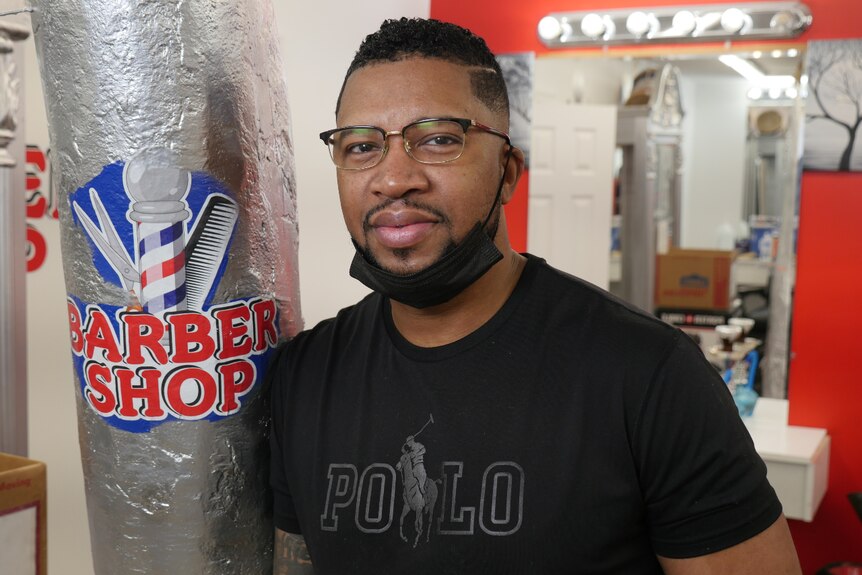 A man in a black shirt with glasses next to a barber shop pole.