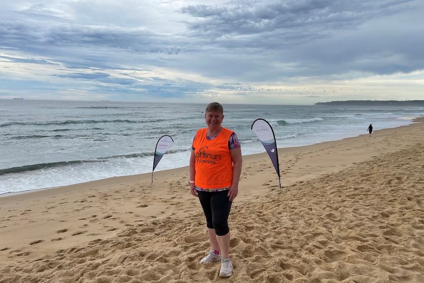 A woman in a park vest on the beach has park signs behind her.