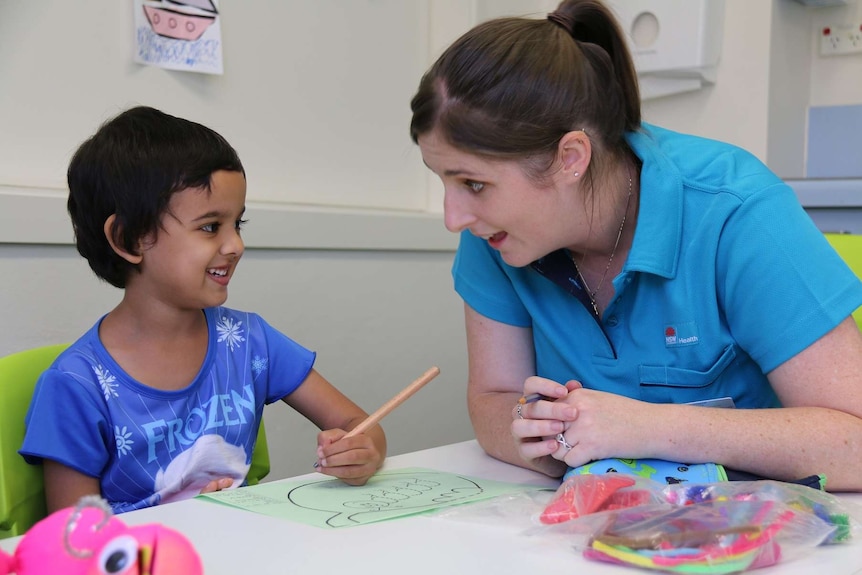 A children draws and looks at a speech pathologist