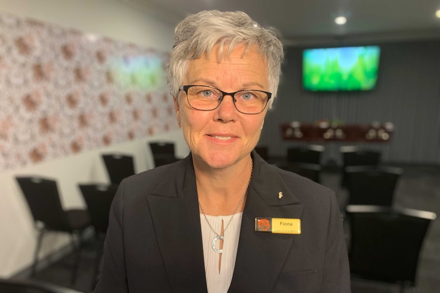 Fiona McDowell wearing a black suit jacket and smiling at the camera in a small funeral chapel.