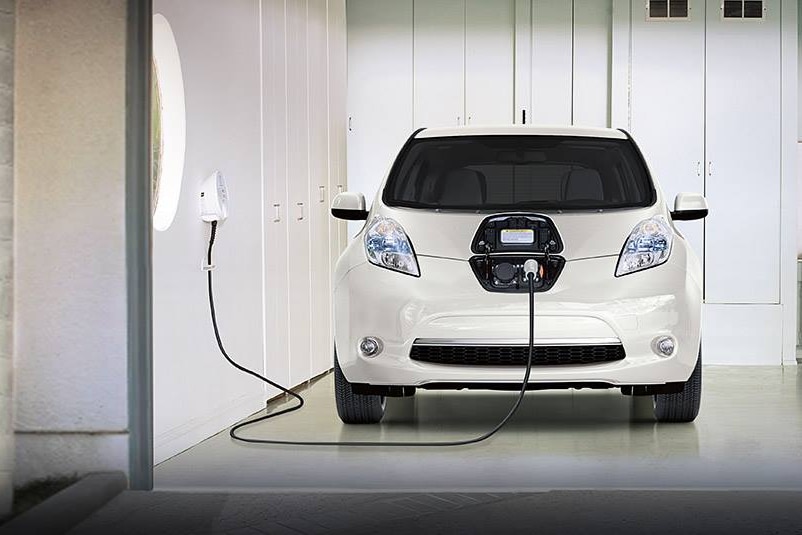 Un pequeño coche eléctrico conectado a un cargador eléctrico dentro de un garaje.