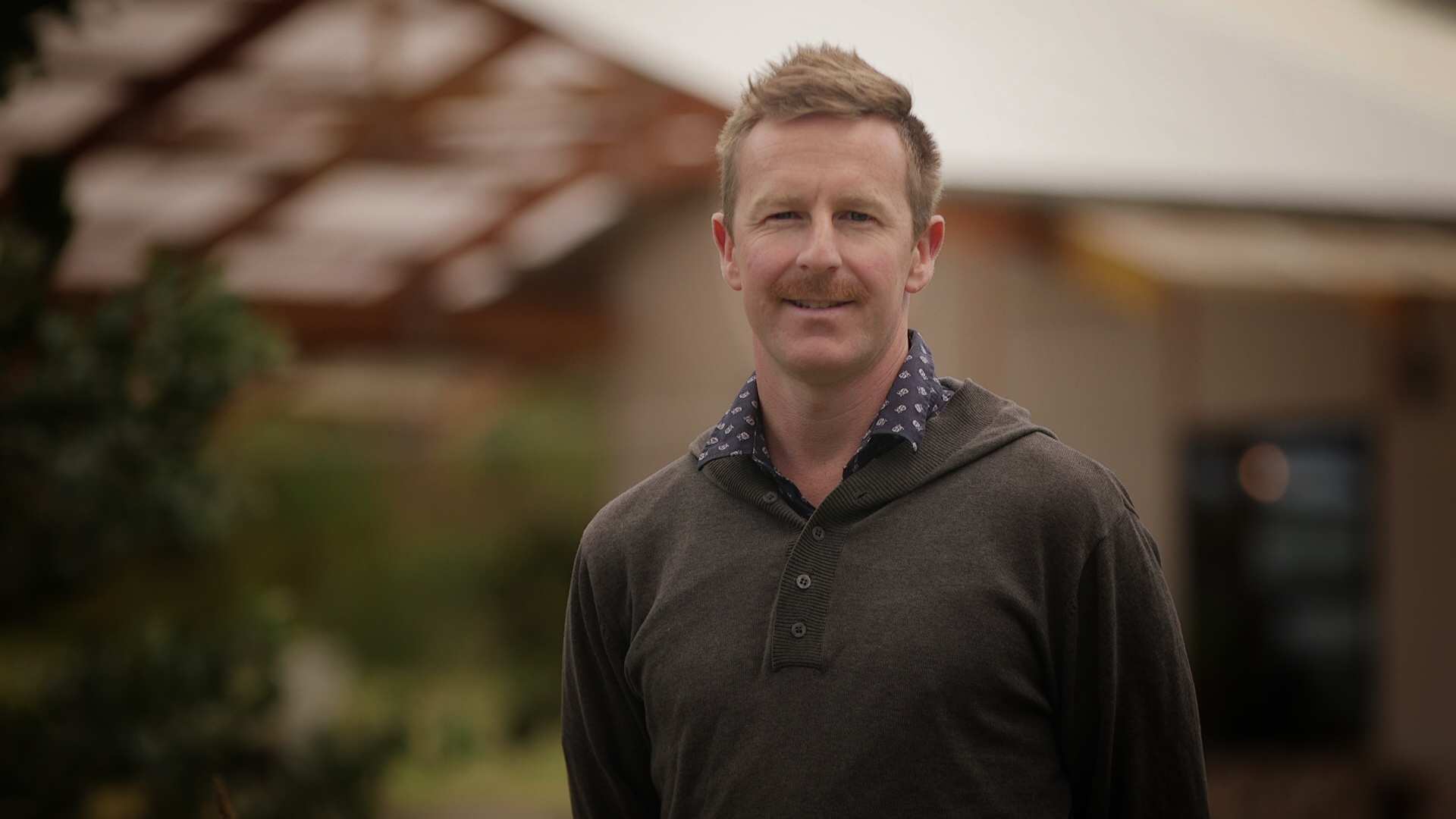 A close-up of a man smiling, his house is out of focus in the background