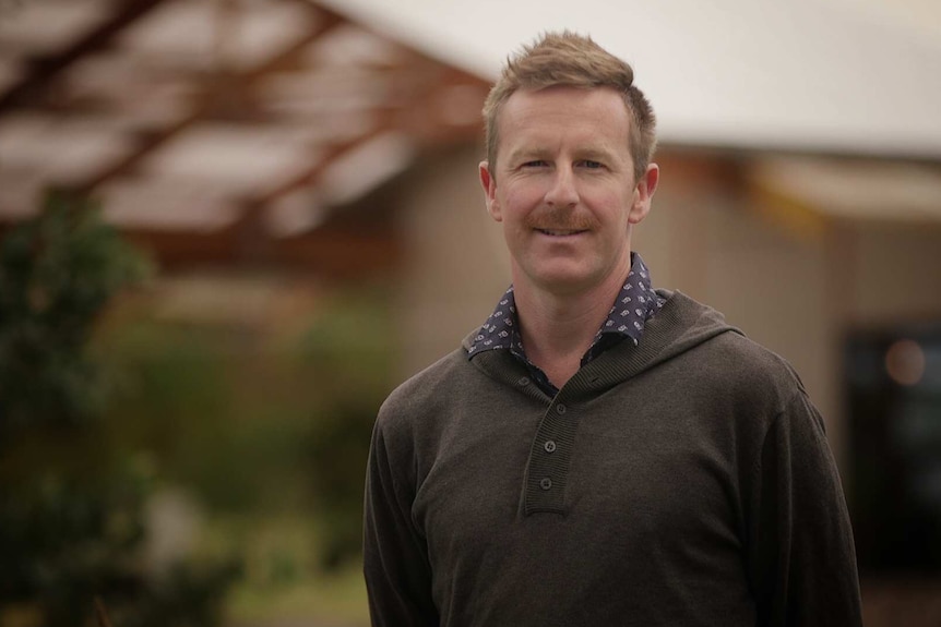 A close-up of a man smiling, his house is out of focus in the background