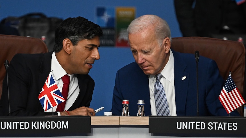 Rishi Sunak and Joe Biden huddle together and have a chat at a summit desk 