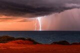 Lightning strikes over the ocean with red dirt in the foreground