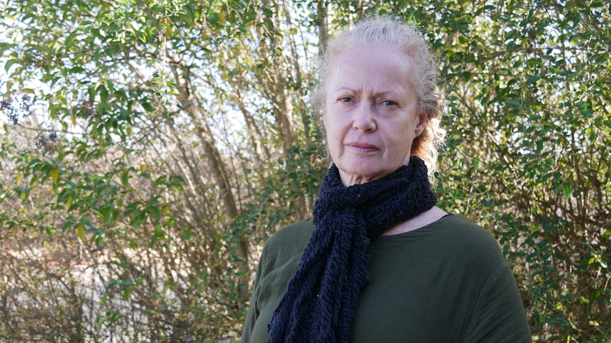 A woman wearing a blue scarf and a green jumper in front of a tree