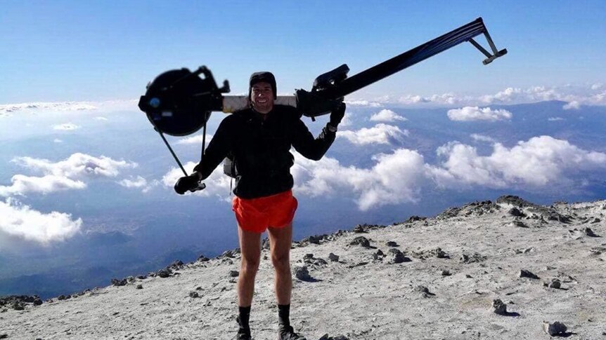 Matthew Paul Disney carries a rowing machine on a moutain.