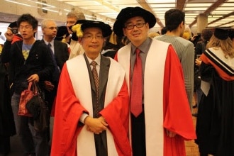 Two Chinese men in red academic robes smiling at the camera.