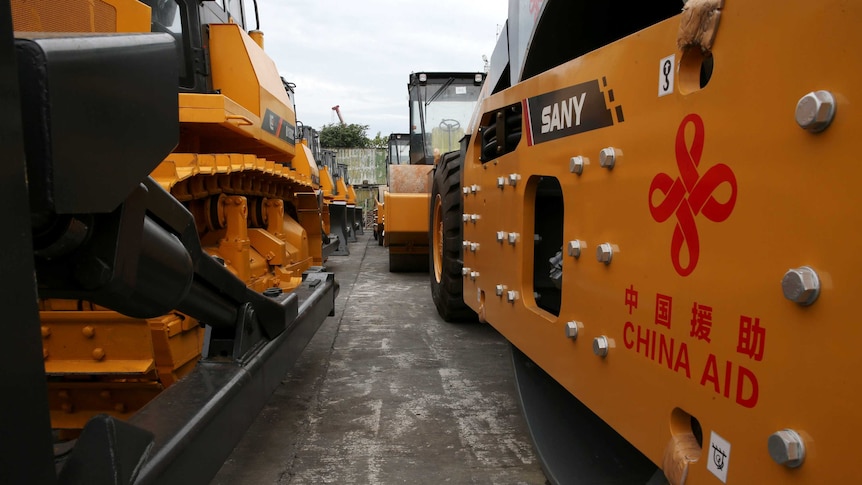 Rows of new construction equipment are seen with "China Aid" written on the side.
