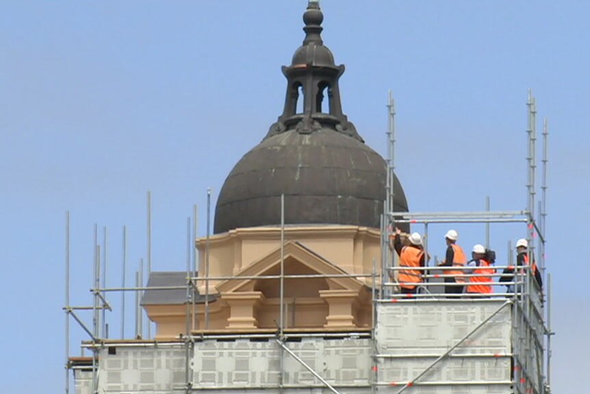 People in hi-vis clothing stand on scaffolding, inspecting the exterior of a dome at Flinders Street Station, November 2017.