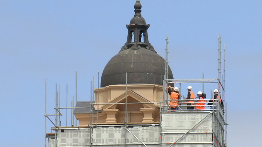 People in hi-vis clothing stand on scaffolding, inspecting the exterior of a dome at Flinders Street Station, November 2017.