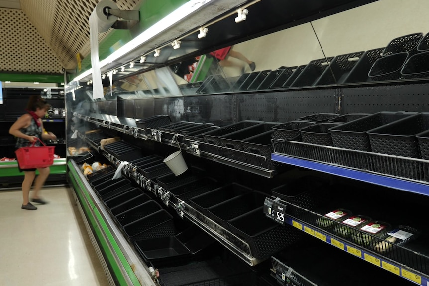 A woman inspects an empty supermarket shelf