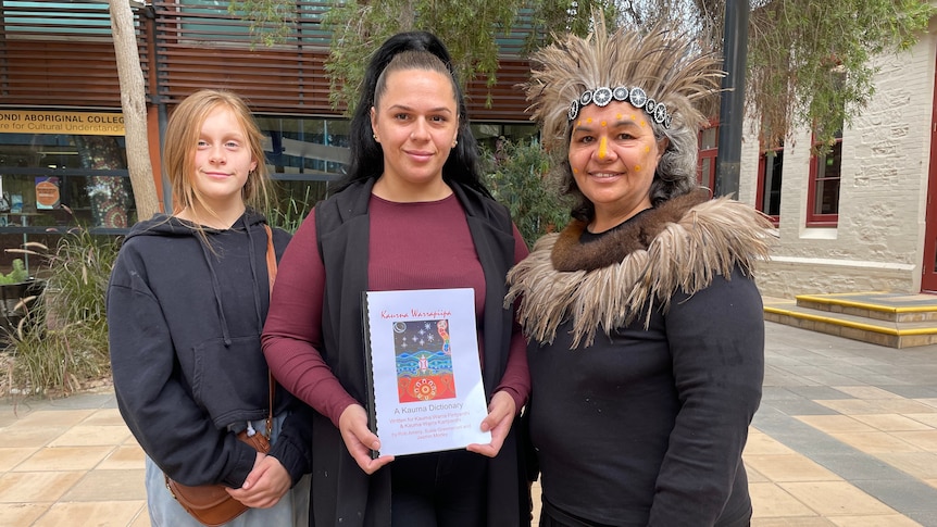 A Kaurna woman holds a dictionary, flanked by family members.