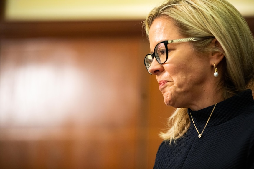 A side profile of a blonde woman with glasses and a black turtleneck