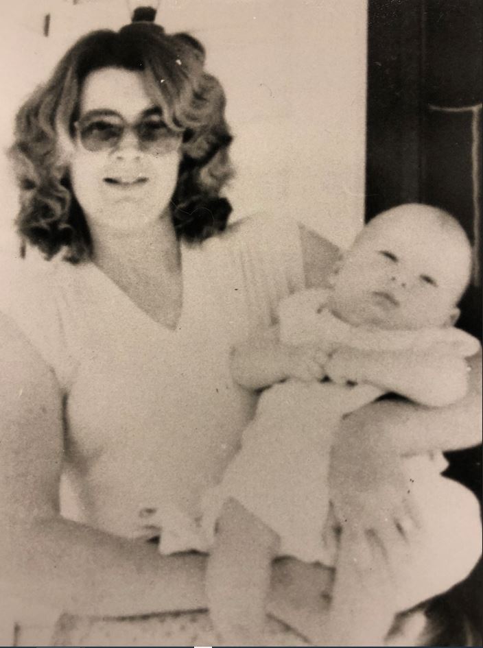 A woman in sunglasses stands holding a baby