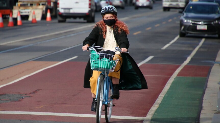 A woman wearing a black face mask and long dark coat riding a bike down the street in Brunswick.