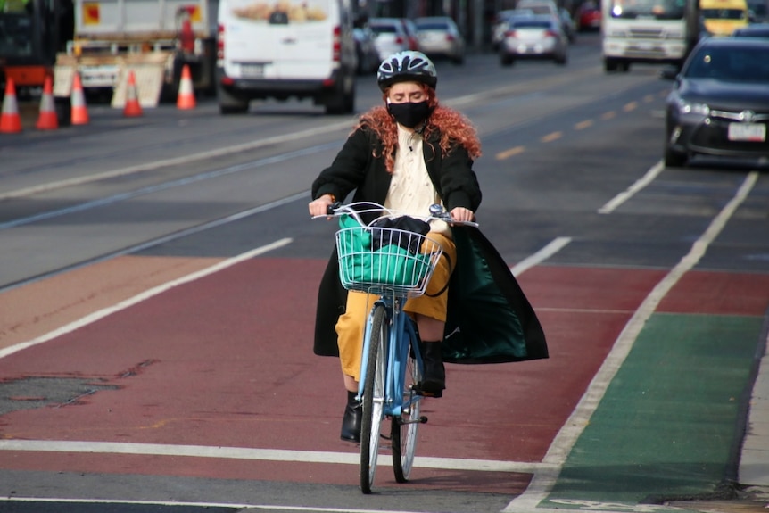 A woman wearing a black face mask and long dark coat riding a bike down the street in Brunswick.