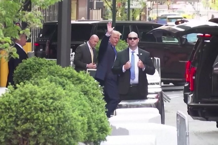Former US persident Donald Trump waves at the camera while walking on the street to a waiting car.