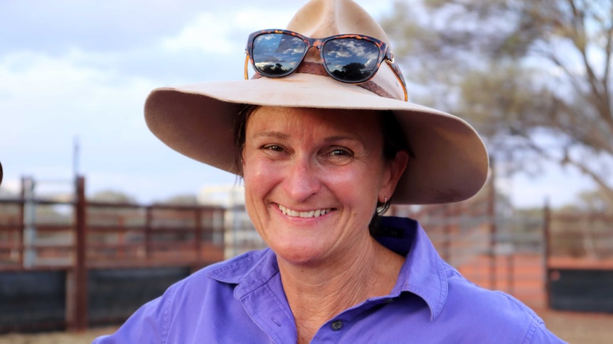 Headshot of a smiling woman in a hat with sunglasses balanced on top.