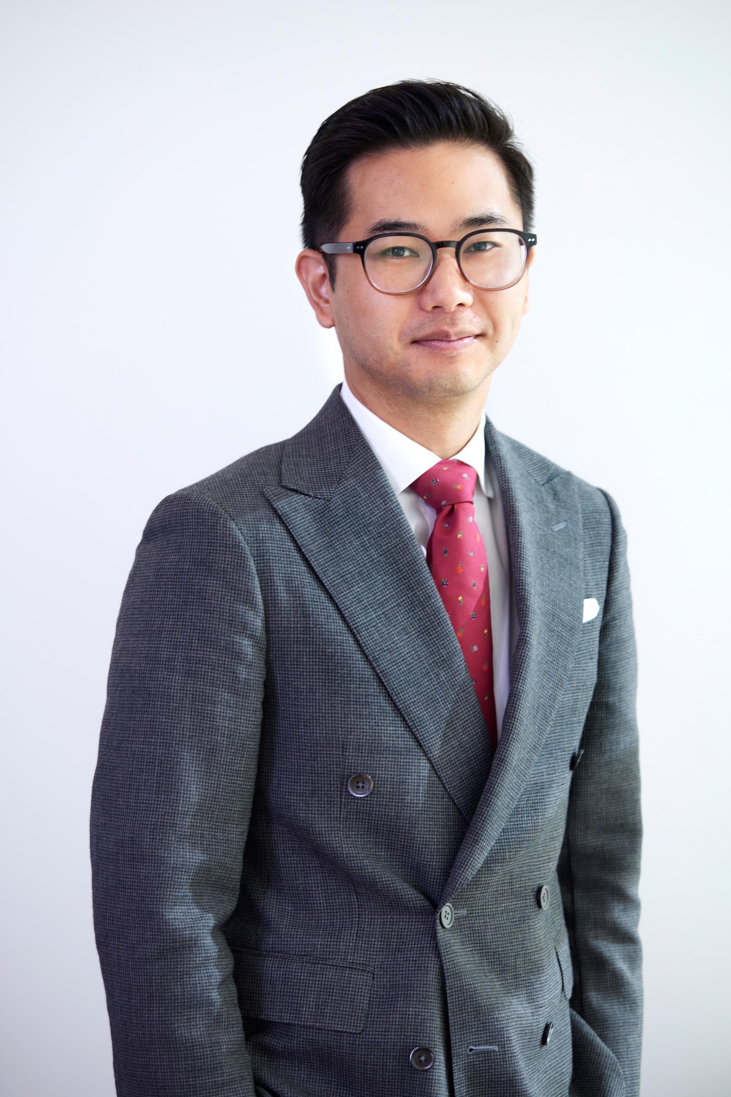 Chadwick tiene cabello negro y gafas, viste traje y corbata roja y sonríe levemente.