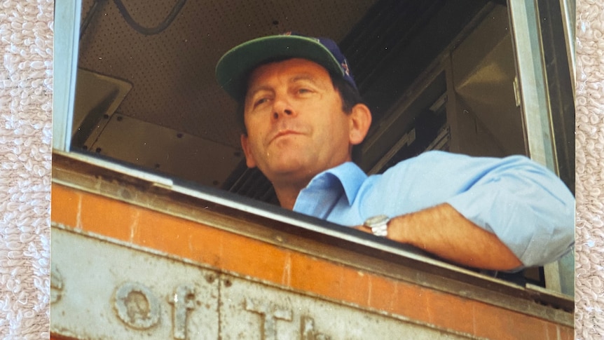 Photo of man wearing cap in the front of a train locomotive.