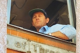 Photo of man wearing cap in the front of a train locomotive.