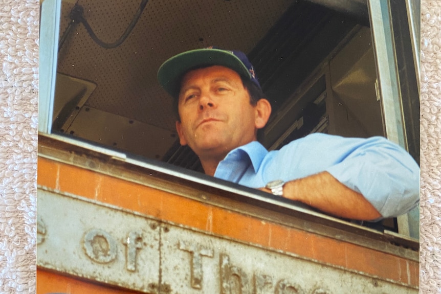 Photo of man wearing cap in the front of a train locomotive.