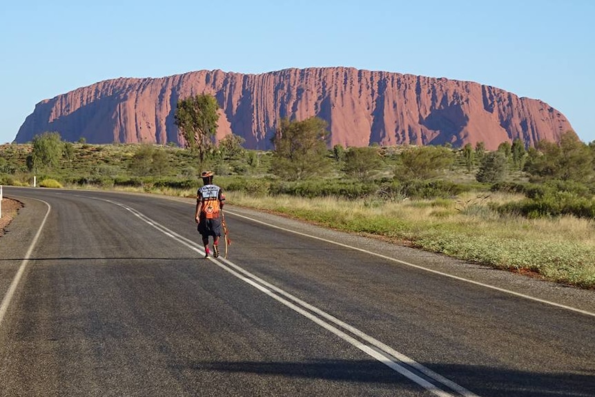 Clinton walks on a road with Uluru in the background.