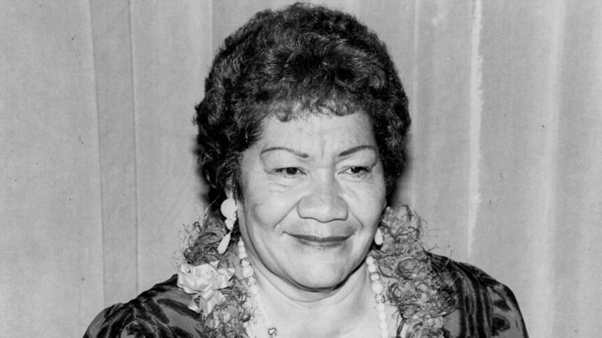 Black and white headshot image of a Samoan woman with short hair. Wears flower lei and pearls around her neck. 