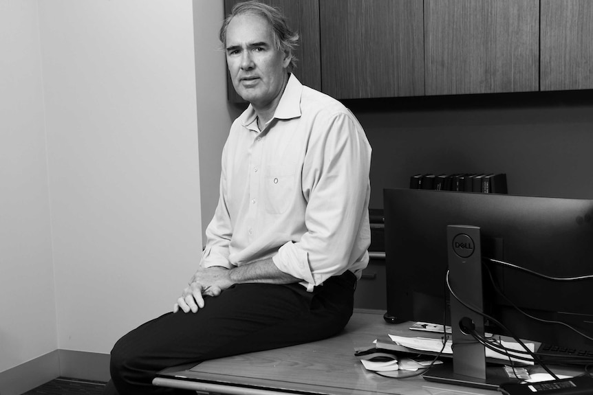 Black and white photo of Jason Kovacic sitting at his desk.