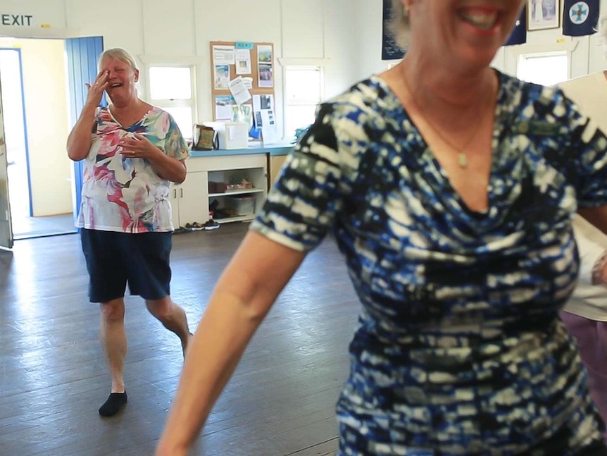 A woman touches her face as she laughs in a ballet class. Women laughing in foreground.