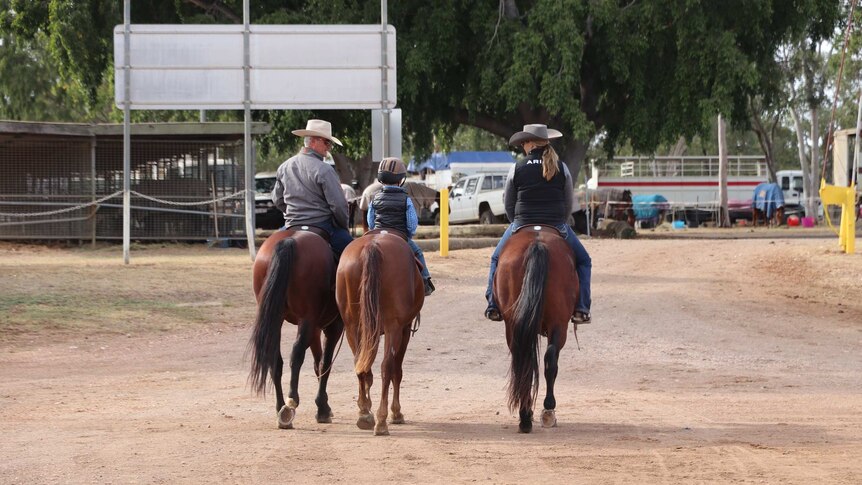 A family riding horse shead back to their camp in the background