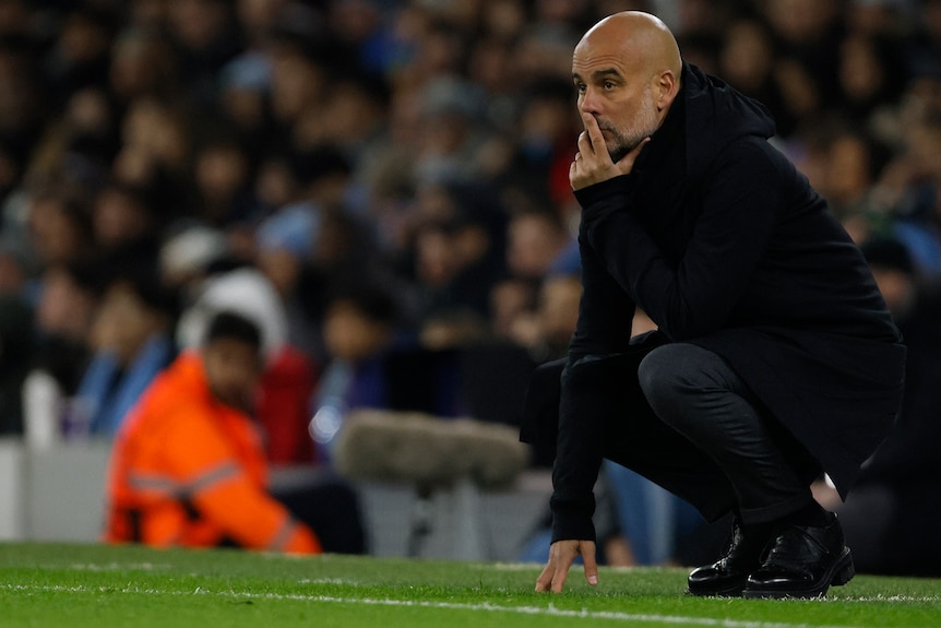 Pep Guardiola crouches during a Champions League match.