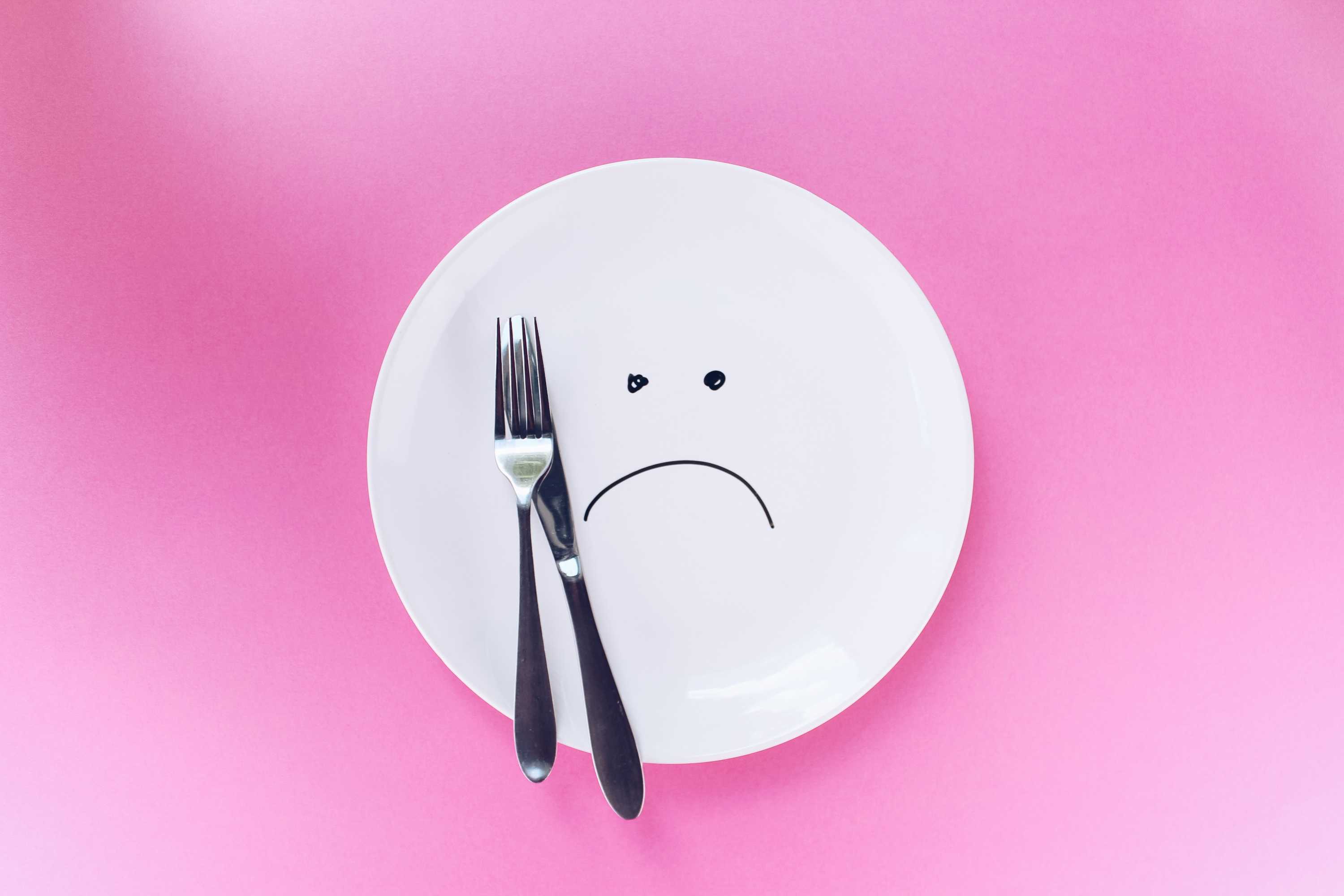 Image of dinner plate with knife and fork and sad face for a story about why we get hangry.