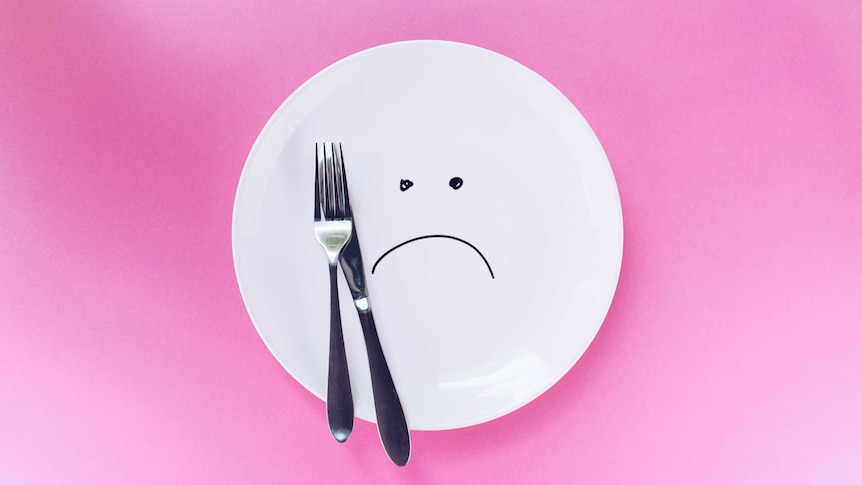 Image of dinner plate with knife and fork and sad face for a story about why we get hangry.