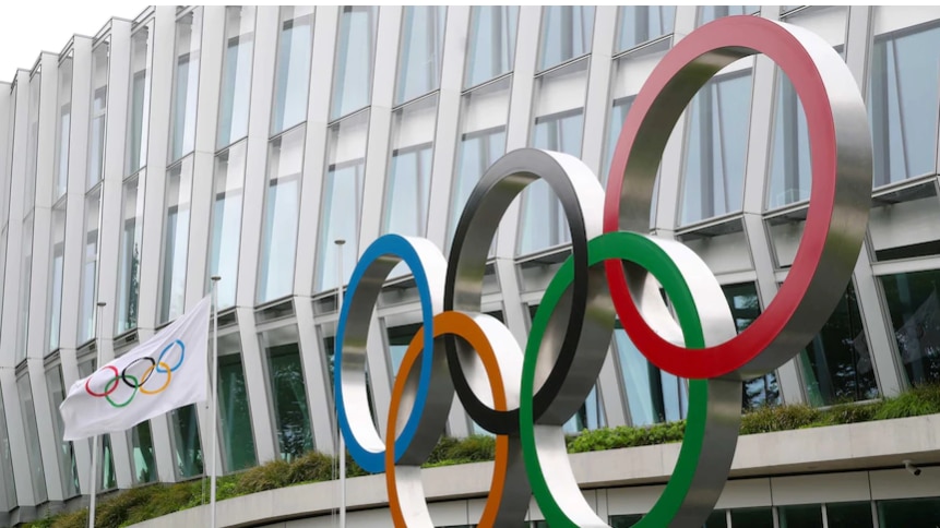 The five coloured rings of the Olympics on the outside of a building with an Olympic flag flying.