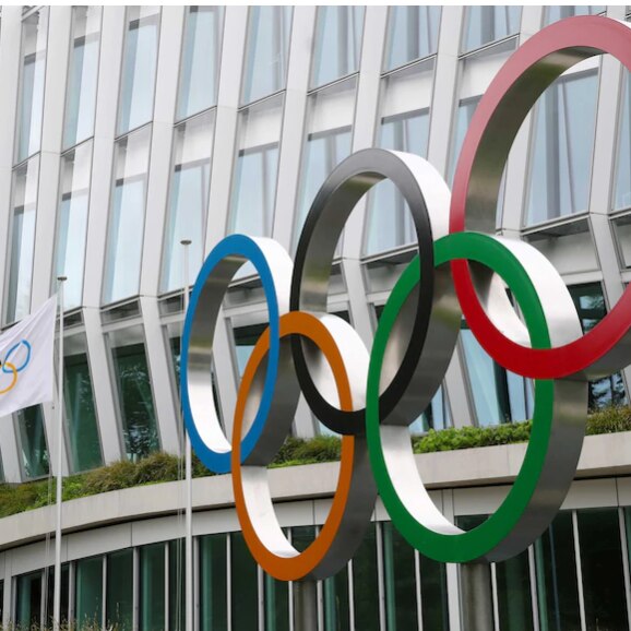 The five coloured rings of the Olympics on the outside of a building with an Olympic flag flying.