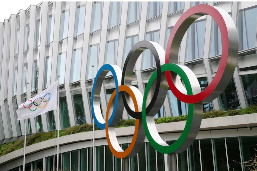 The five coloured rings of the Olympics on the outside of a building with an Olympic flag flying.