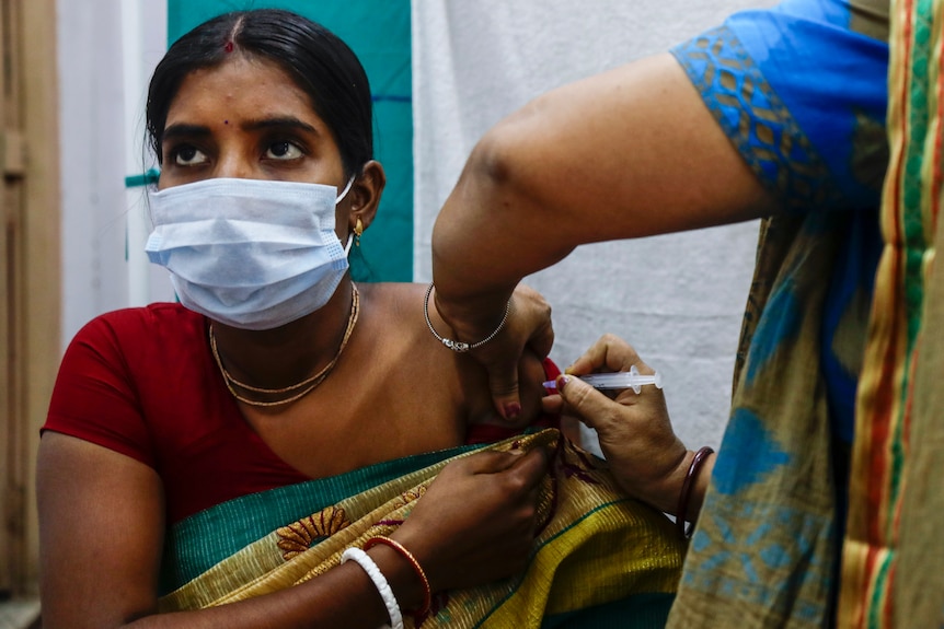 Una donna indiana che indossa una maschera riceve un'iniezione di un vaccino contro il COVID-19.  