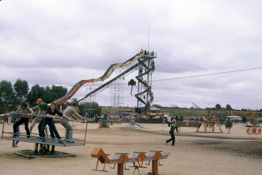 A playground in the 1980s with bare dirt on ground and lots of people.