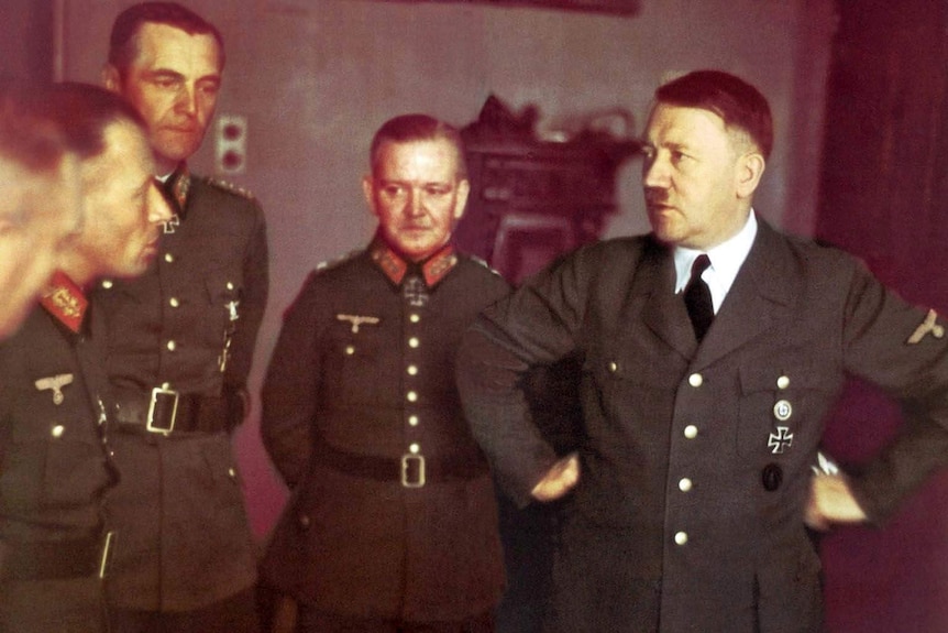 Three German generals in uniform standing next to Adolf Hitler who has his hands on his hips