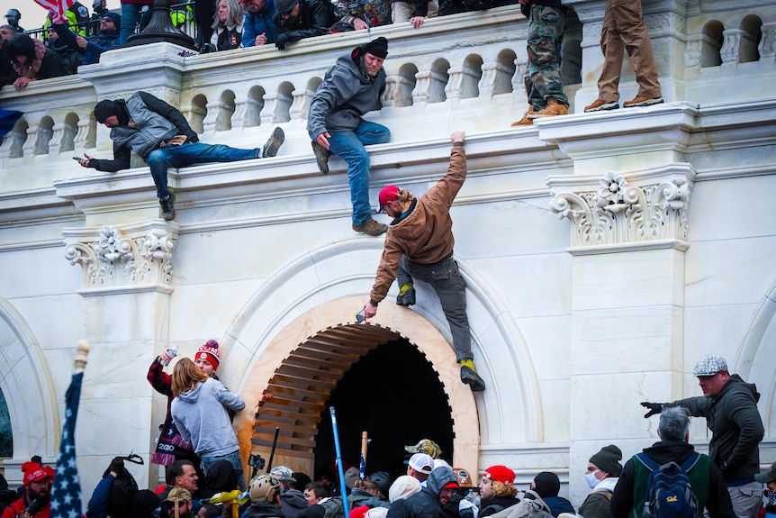 Three men climb up a marble wall as a crowd gathers below