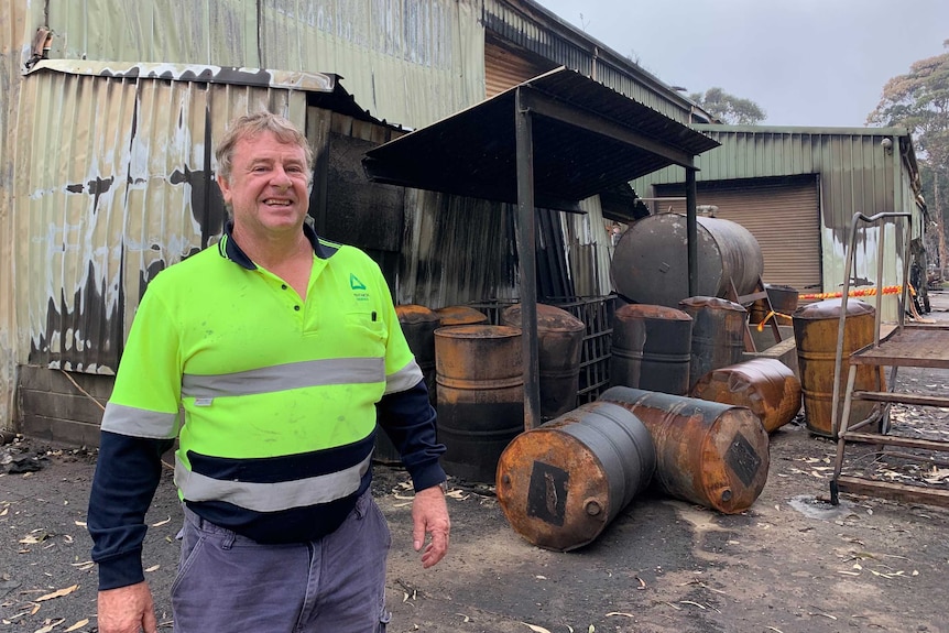 Employee Trevor Smith stands smiling next to a burnt out shed