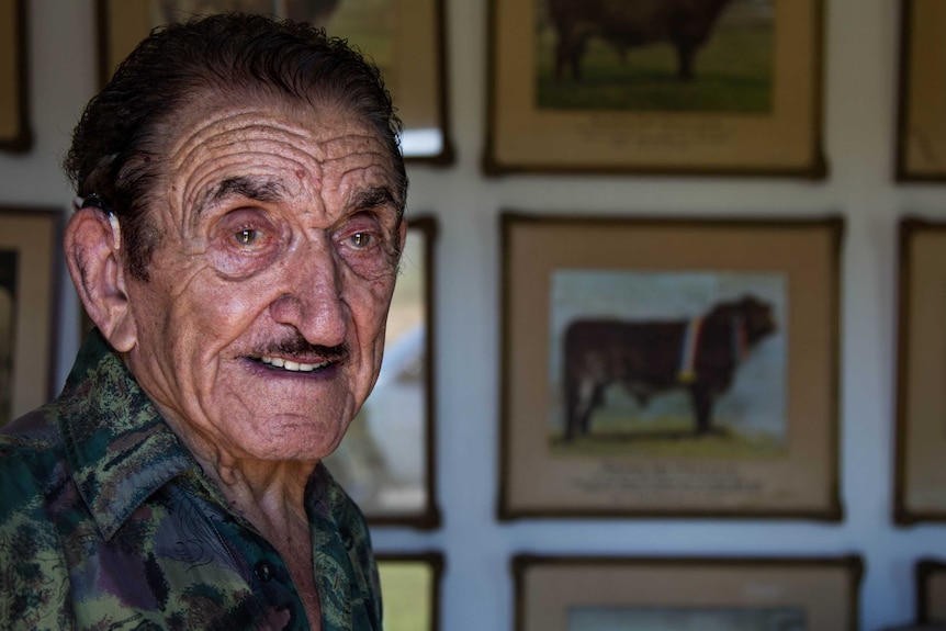 Rick Pisaturo stares into distance with wall of photos behind him.